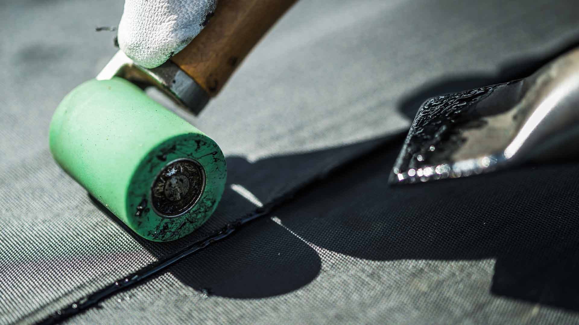 Close-up of a roller and hot-air tool sealing a roofing membrane