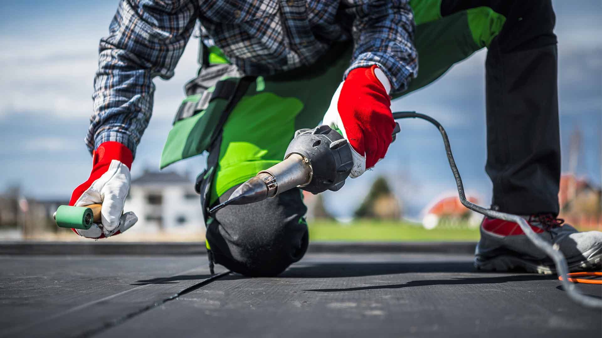 Roofer sealing a flat roof membrane with a heat gun and roller