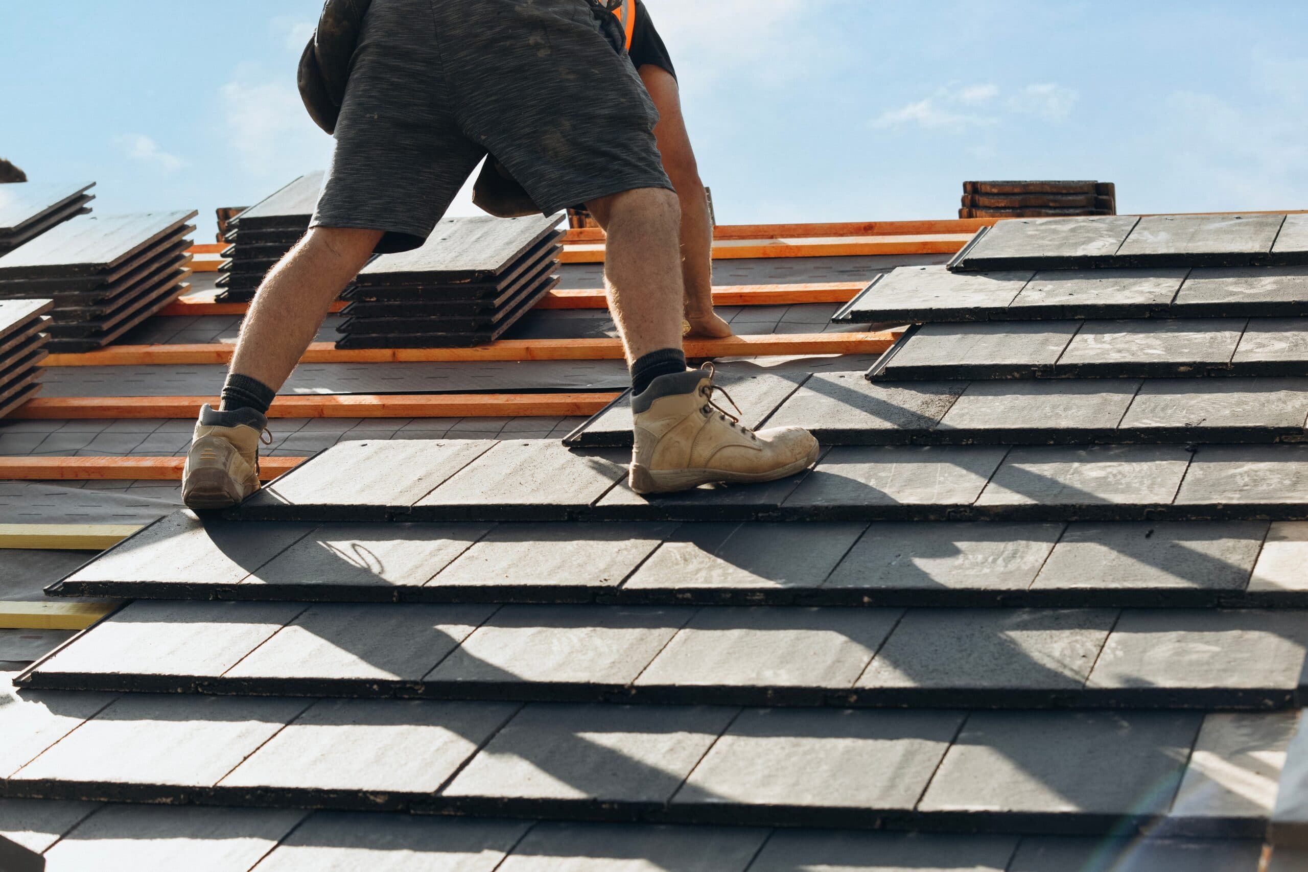 A roofer laying slate tiles on timber roof battens