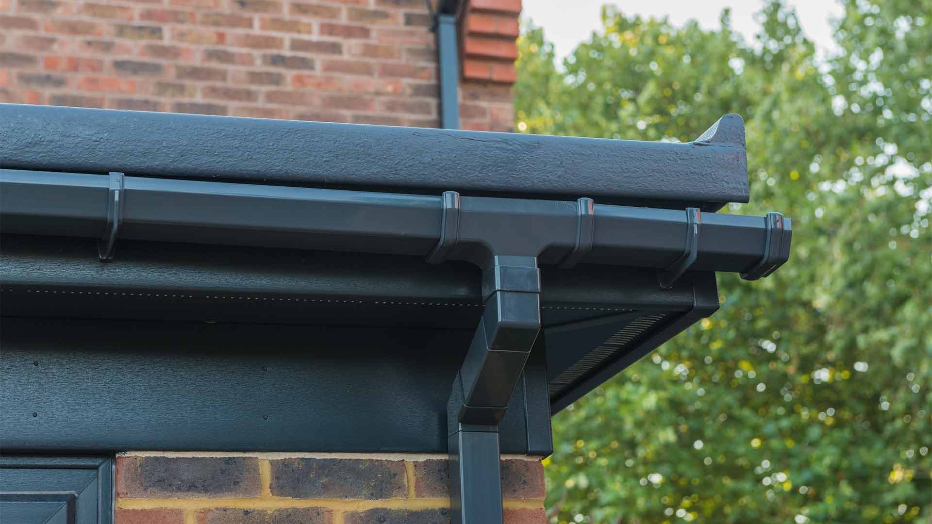 Dark guttering, fascia and downpipe at the edge of a flat roof