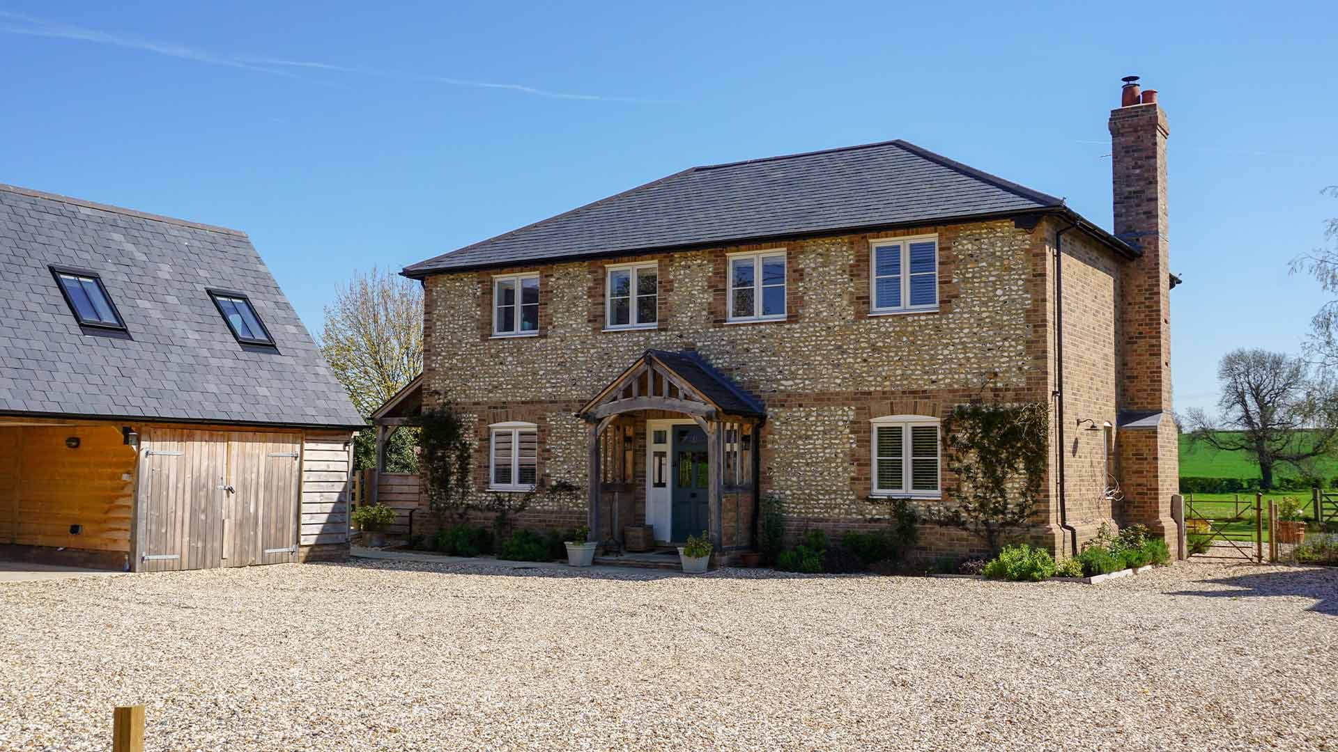 Stone house and timber outbuilding with slate roofs under a clear blue sky