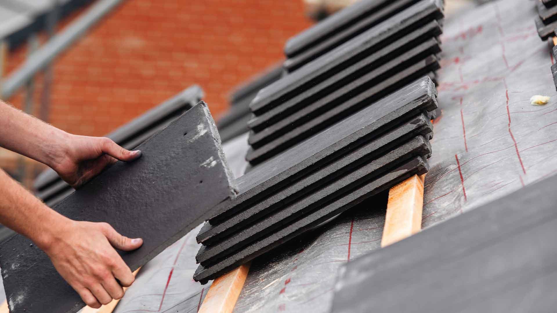 Roofer positioning a dark roof tile over timber battens and roofing membrane